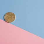 A single gold Bitcoin on a minimal pastel blue and pink background. — Crypto Profits Through Strategic Bitcoin Futures Tradin