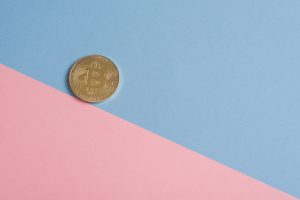 A single gold Bitcoin on a minimal pastel blue and pink background. — Crypto Profits Through Strategic Bitcoin Futures Tradin
