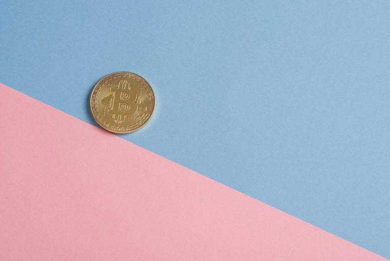 A single gold Bitcoin on a minimal pastel blue and pink background. — Crypto Profits Through Strategic Bitcoin Futures Tradin