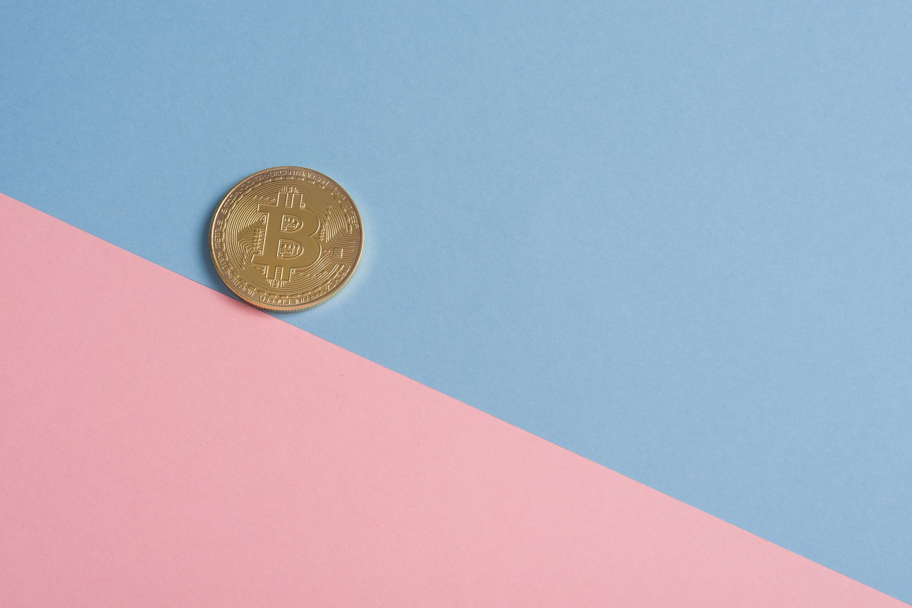 A single gold Bitcoin on a minimal pastel blue and pink background. — Crypto Profits Through Strategic Bitcoin Futures Tradin