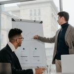 Two businessmen discussing data on a flipchart in a contemporary office setting. — From Beginner to Expert: White Label Faceb