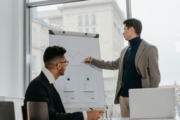 Two businessmen discussing data on a flipchart in a contemporary office setting. — From Beginner to Expert: White Label Faceb