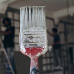Detailed close-up of a paintbrush with men painting a wall in the blurred background, highlighting renovation work. — Staging