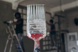 Detailed close-up of a paintbrush with men painting a wall in the blurred background, highlighting renovation work. — Staging