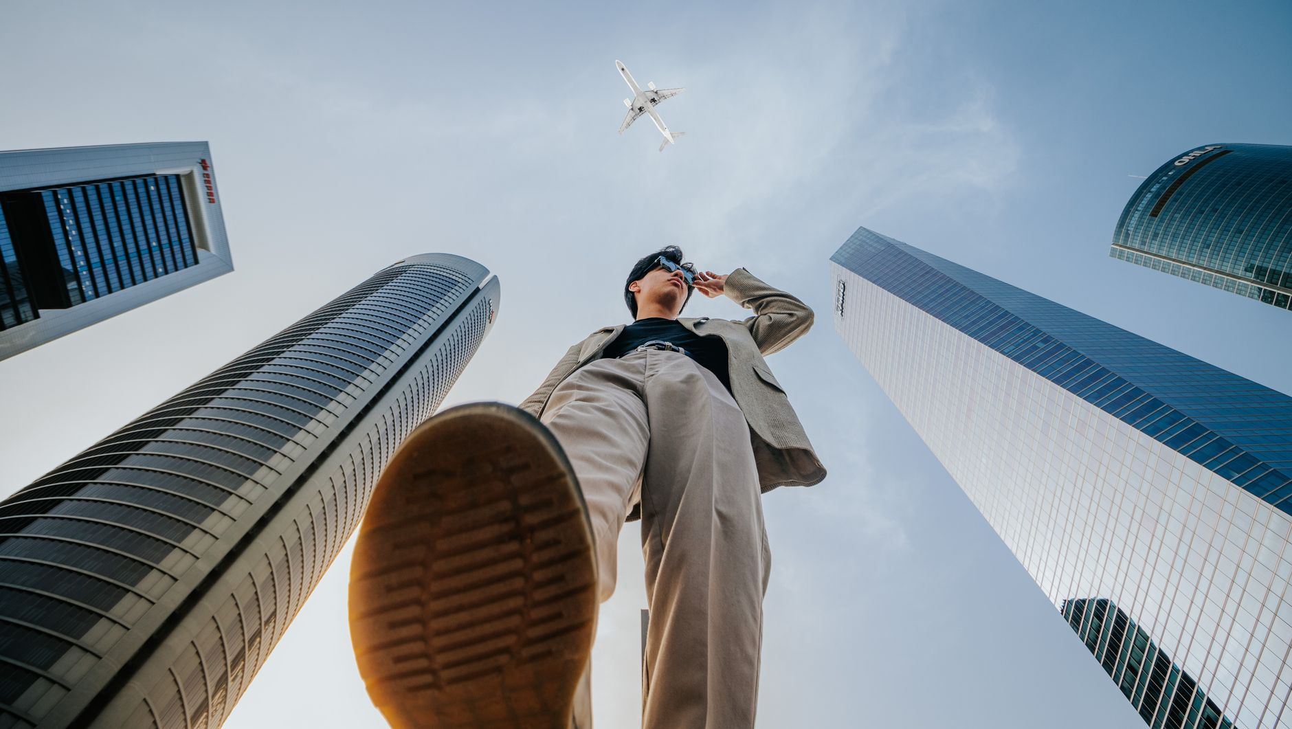Low-angle shot of a man in a suit framed by skyscrapers and a passing airplane. — The Advantages of Proprietary Trading for P