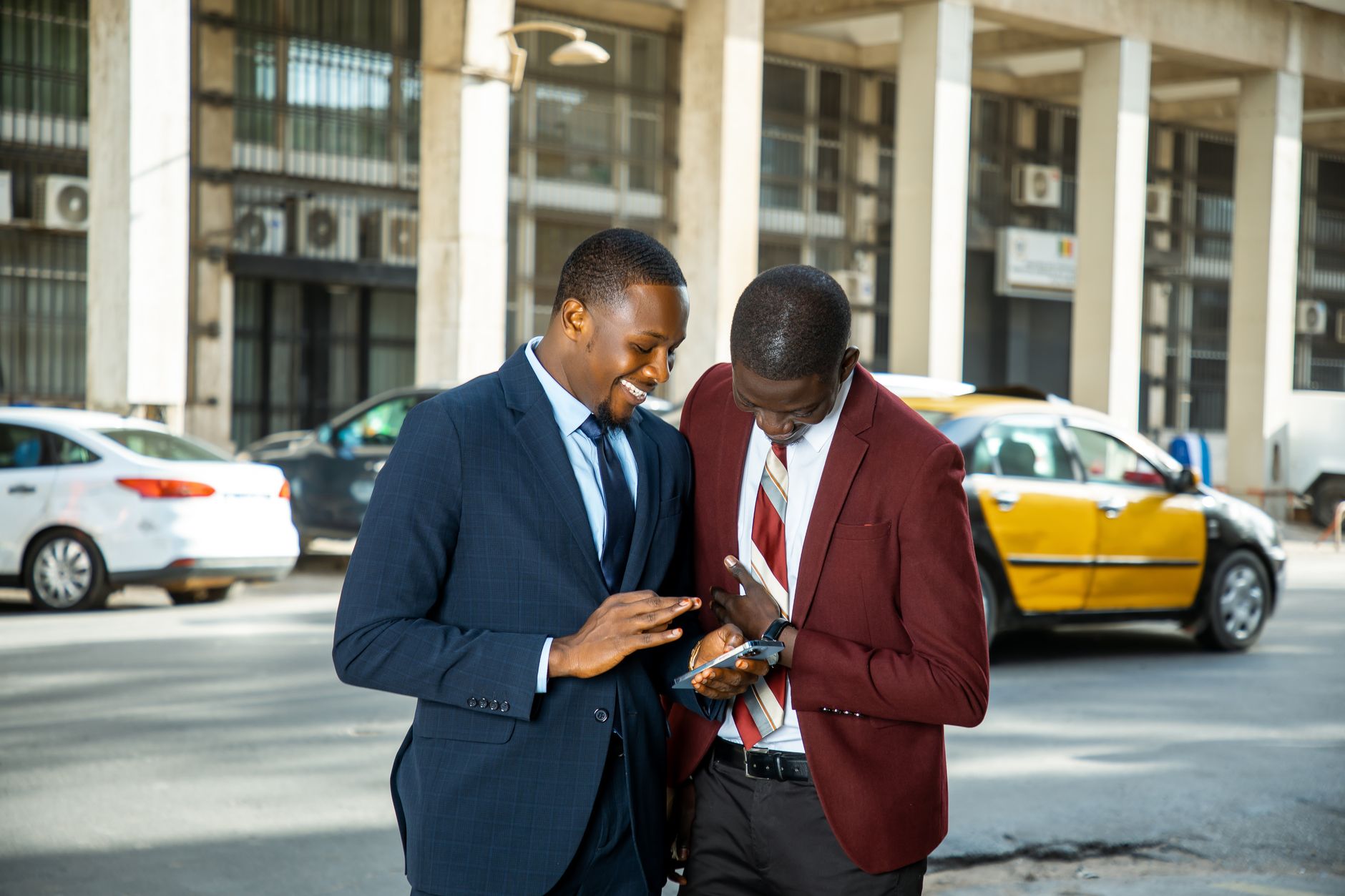 Two businessmen in suits engaging with a mobile phone on a busy street in Dakar. — Top Construction Management Software Tools